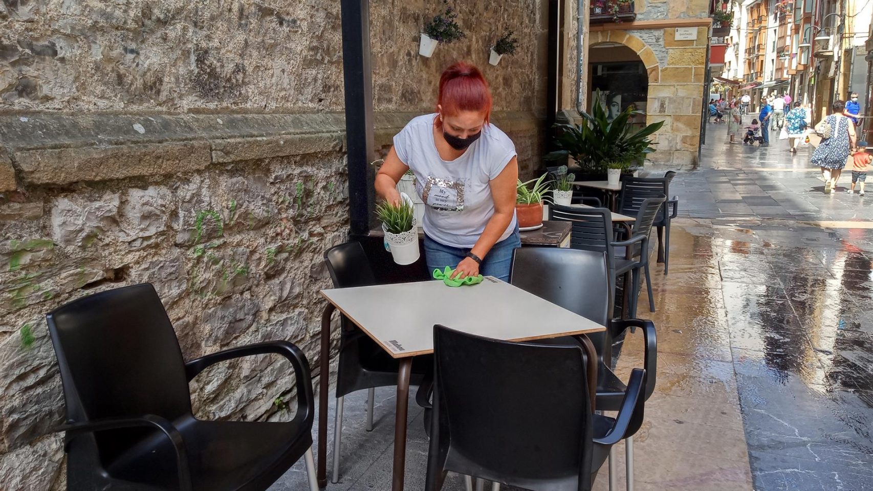 Una mujer desinfecta las mesas de la terraza de un bar.