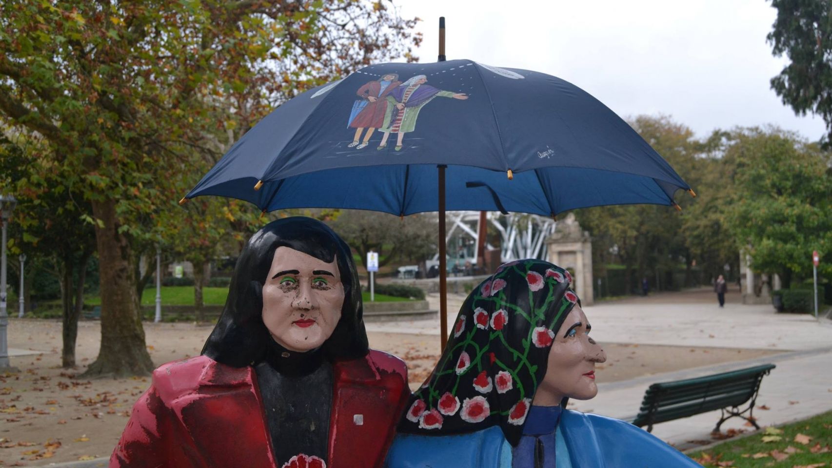 As Marías, obra de César Lombera, resguardándose de la lluvia con un paraguas inspirado en ellas.
