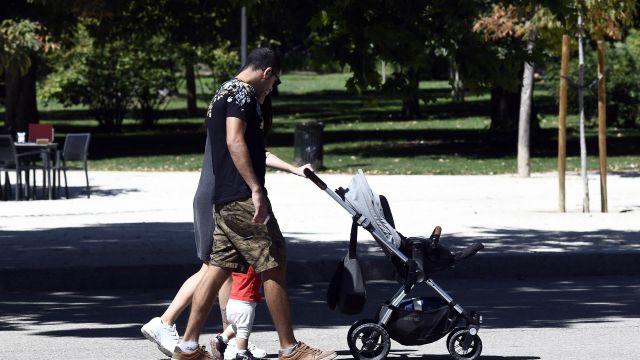 Una pareja y su bebé empujan el carrito del mismo en un parque de Madrid.