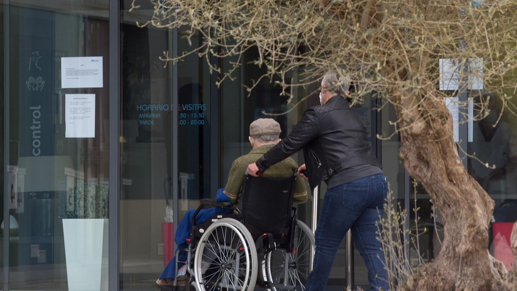Una mujer pasea junto a un anciano en silla de ruedas.