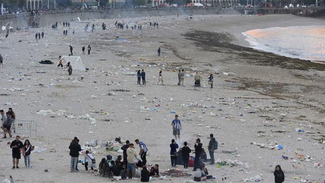 Vista general de la playa de Orzán con grupos de personas y restos de basura después de la celebración de las hogueras de la noche de San Juan.