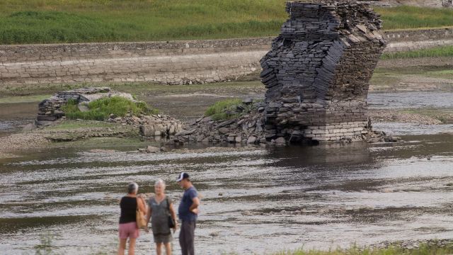 Tres personas junto al río Miño, cuyo bajo caudal ha dejado a la vista las ruinas del antiguo Portomarín.