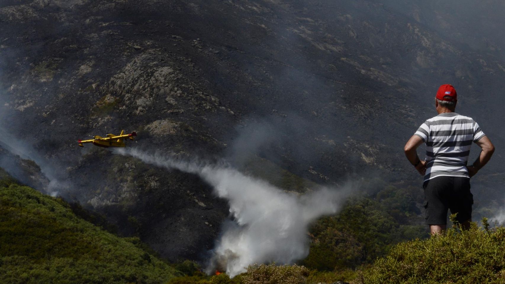 Un vecino de Senderiz en Lobeira observa un hidroavión trabajar en el incendio forestal en la Serra do Leboreiro, en el parque natural de Baixa Limia e Serra do Xurés.