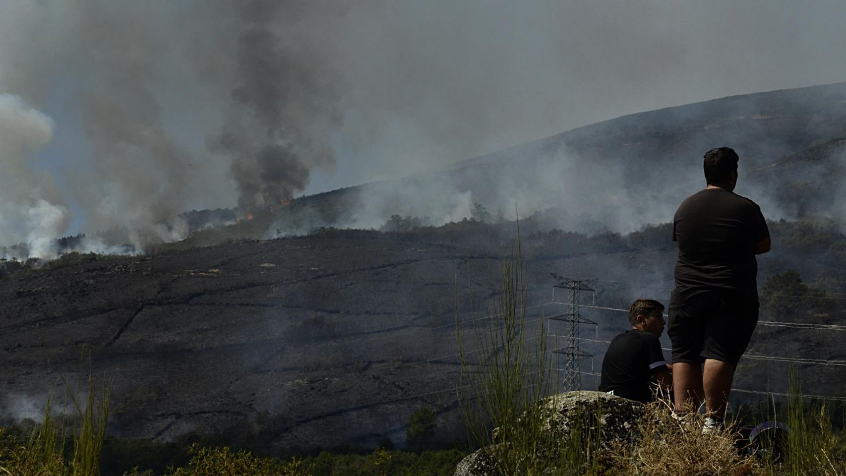 Dos personas de Grou observan el incendio forestal en la Serra do Leboreiro, en Senderiz, en el parque natural de Baixa Limia e Serra do Xurés.