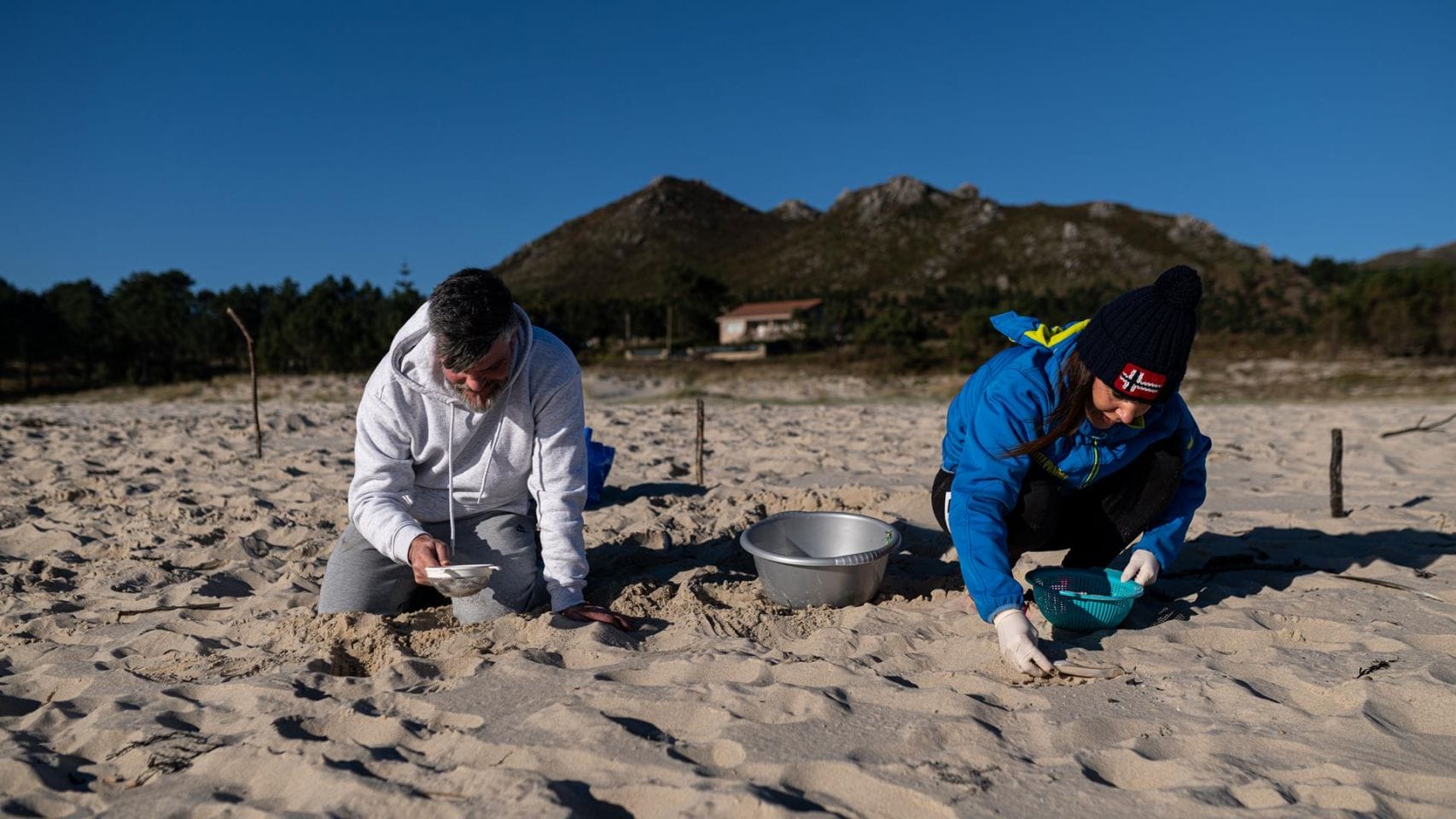 Dos personas recogen pellets de la arena en A Coruña.