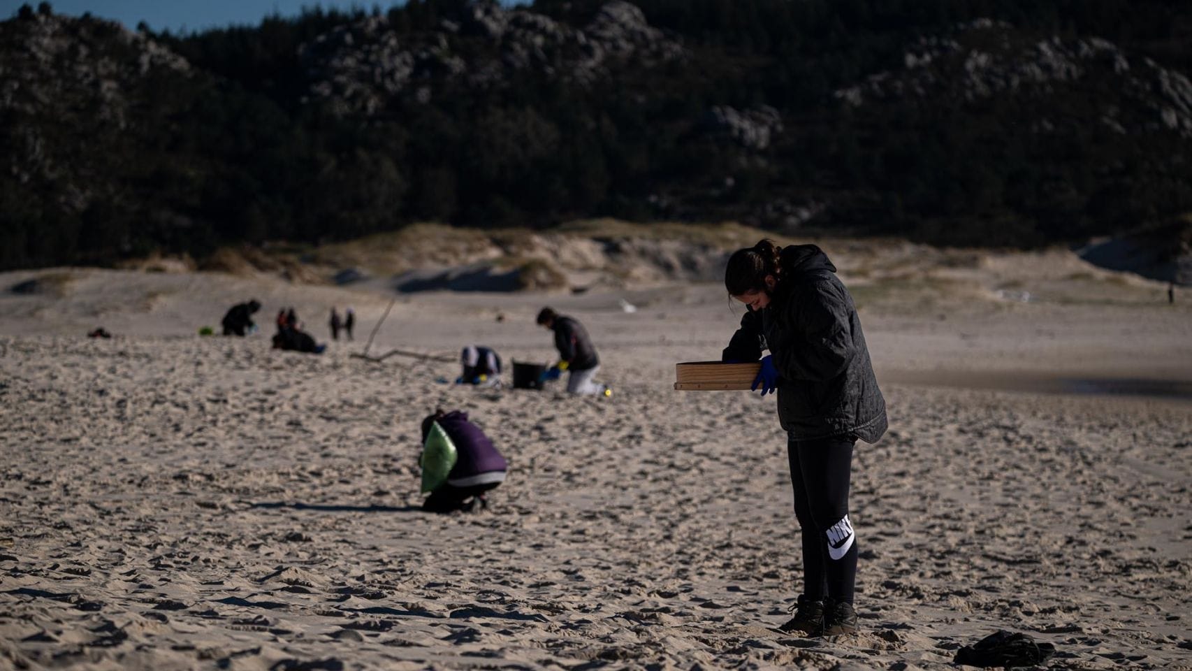 Voluntarios participan en la recogida de pellets de plástico en una playa de Muros.